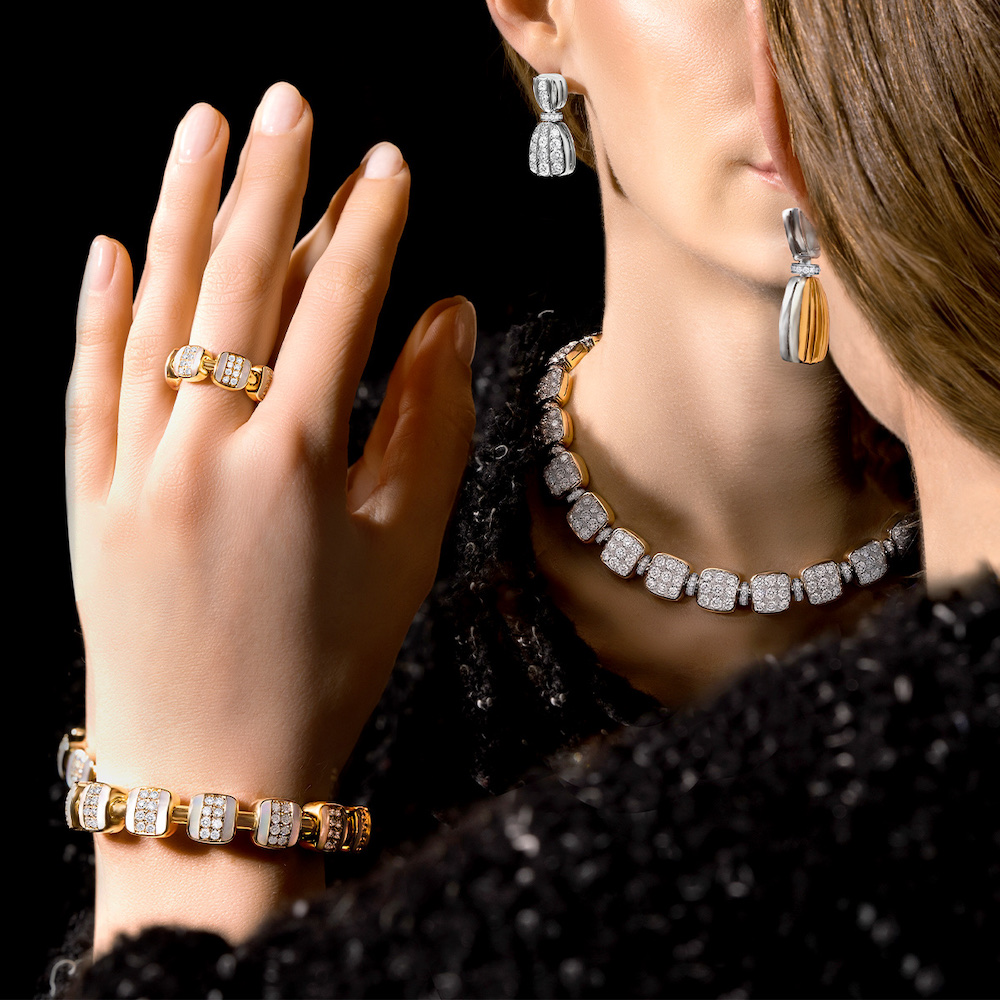 Model looking into a mirror while wearing gold and diamond Reversible Xpandable ring and bracelet, as well as Reversible earrings and necklace. These designs easily flip over with a gentle twist to reveal a completely different design on the reverse – in this case, the diamond flip to reveal and all-gold style for maximum versatility and wearability.